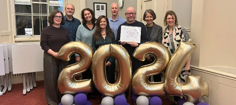 James Smith with colleagues standing in front of 2024 balloons at his leaving reception